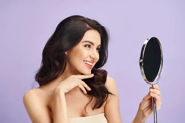 Mulher em vestido sem alças olha para si mesma no espelho enquanto aplica maquiagem. — Fotografia de Stock