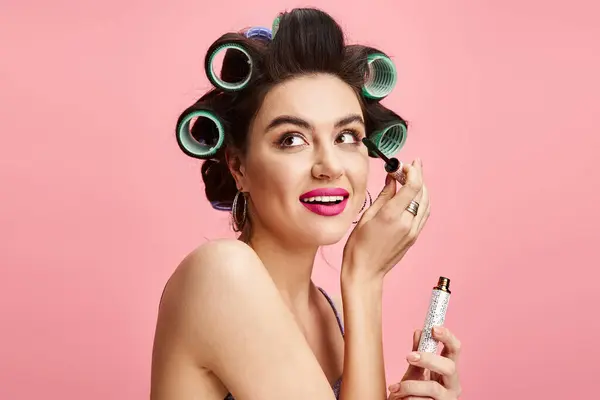 Stylish woman with curlers in hair holding maskara, applying makeup. — Stock Photo