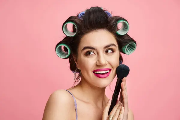 Une femme avec des bigoudis dans ses cheveux tient un pinceau, mettant en valeur sa routine beauté. — Photo de stock