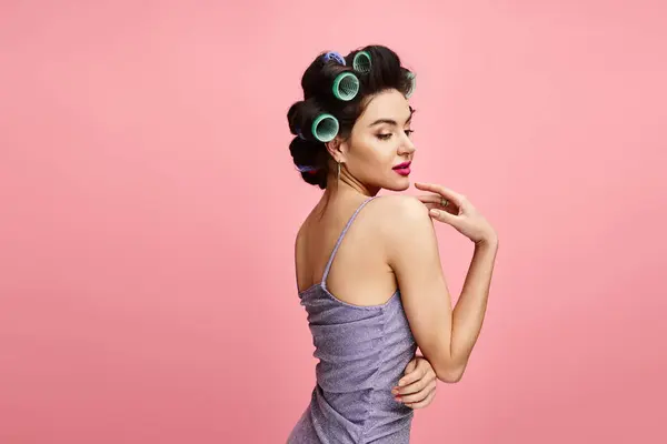 Une femme étonnante dans un élégant haut violet, coiffant ses cheveux avec des rouleaux verts. — Photo de stock