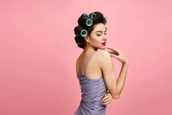 A stunning woman in an elegant purple top, styling her hair with green rollers. — Stock Photo