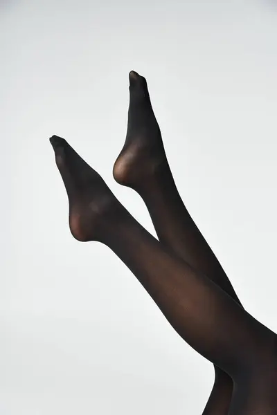 A young woman showcasing her legs in black stockings against a grey studio backdrop. — Stock Photo