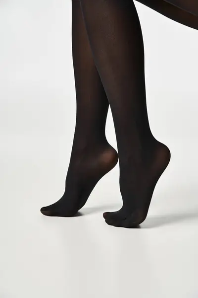 Uma jovem mulher mostra suas pernas em meias pretas elegantes contra um fundo de estúdio cinza neutro. — Fotografia de Stock