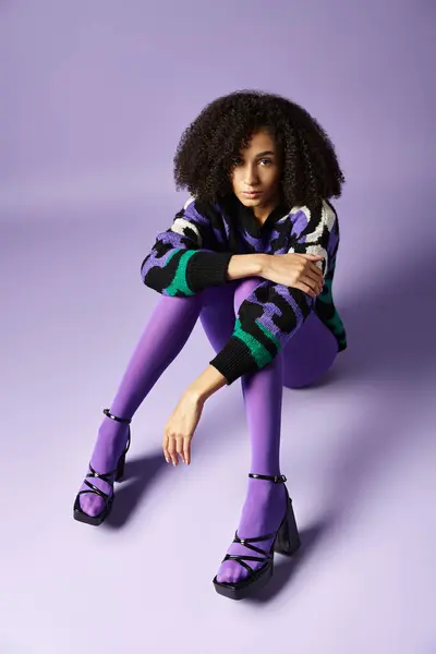 A dark skinned young woman wearing vibrant purple and green clothes is sitting on the ground. — Stock Photo