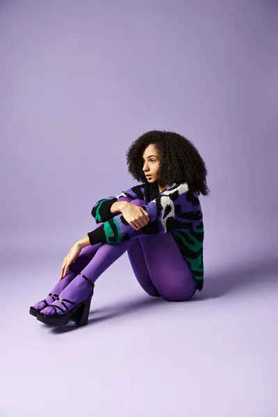 Young woman in vibrant tights and sweater sits gracefully on the ground against a purple background. — Stock Photo