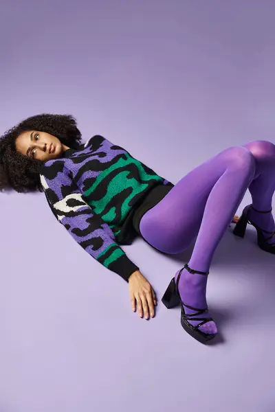 A young woman laying gracefully on the ground, styled in vibrant tights, against a purple backdrop in a studio. — Stock Photo