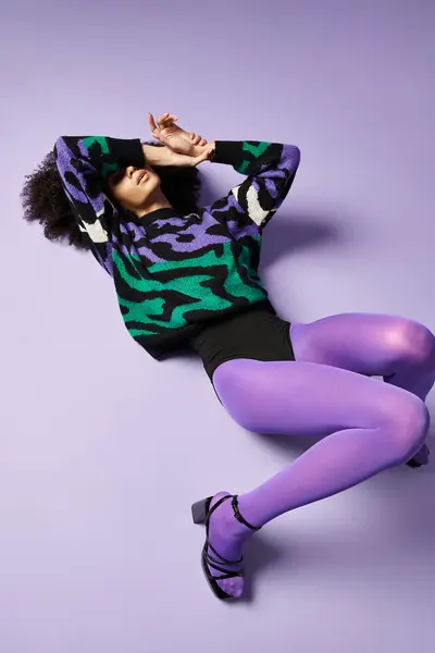 A young woman in vibrant tights and sweater laying gracefully on a purple ground in a studio setting. — Stock Photo