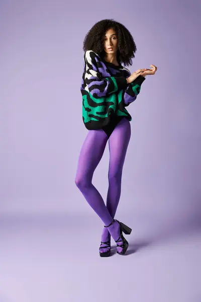 A young woman strikes a pose in a vibrant purple and green outfit against a striking purple background in a studio setting. — Stock Photo