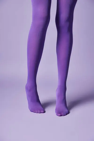 Une jeune femme en bas violets vibrants frappant une pose sur un fond violet dans un studio. — Photo de stock