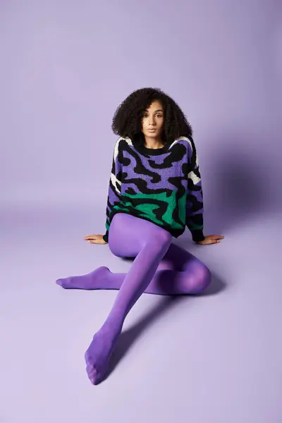 Молодая женщина в ярких колготках и свитере сидит скрестив ноги на фиолетовом фоне в спокойной и расслабленной позе. — стоковое фото