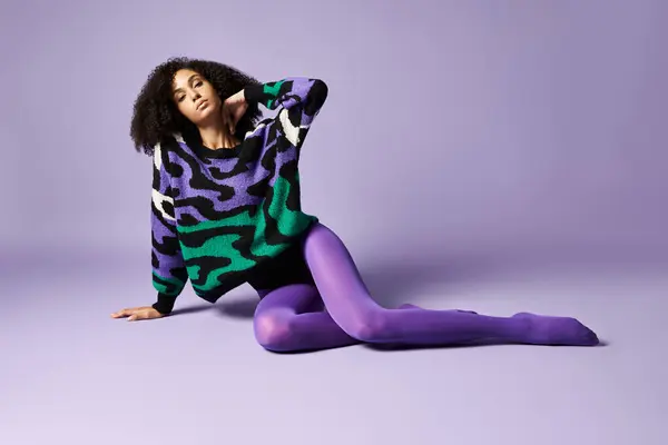 A young woman wearing purple tights and a sweater sitting on the ground in a studio with a purple background. — Stock Photo