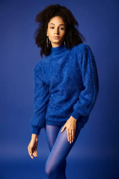 Молодая женщина изящно позирует в ярком голубом свитере и колготках на фоне в студии. — стоковое фото