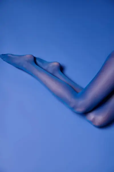 Una giovane donna posa con collant vivaci contro un vivido sfondo blu, in mostra le gambe. — Foto stock