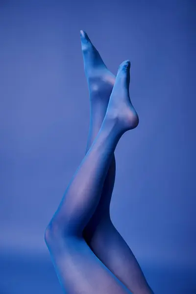 A young womans legs are elegantly highlighted by blue light, wearing vibrant tights and a sweater, posed in a studio. — стоковое фото