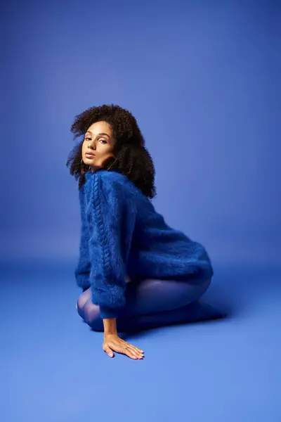 Uma jovem mulher em meias vibrantes e suéter senta-se no chão contra um impressionante fundo azul. — Fotografia de Stock