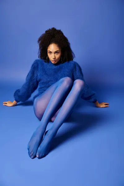 Молодая женщина в ярких колготках и свитере сидит на полу в студии на синем фоне. — стоковое фото