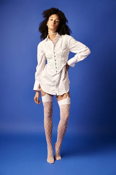 Una joven mujer exuda elegancia y gracia mientras posa con medias blancas y un vestido sobre un fondo azul del estudio. - foto de stock