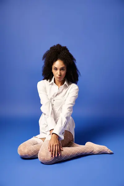 A young woman dressed in white sits on the ground with her legs crossed, exuding peace and elegance in a studio setting. — Stock Photo