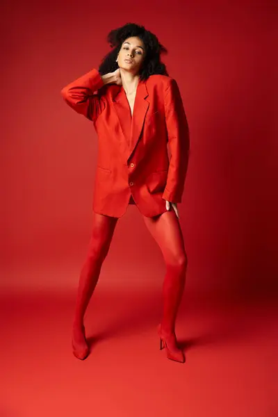 Une jeune femme en costume rouge saisissant pose pour une photo professionnelle dans un studio animé. — Photo de stock