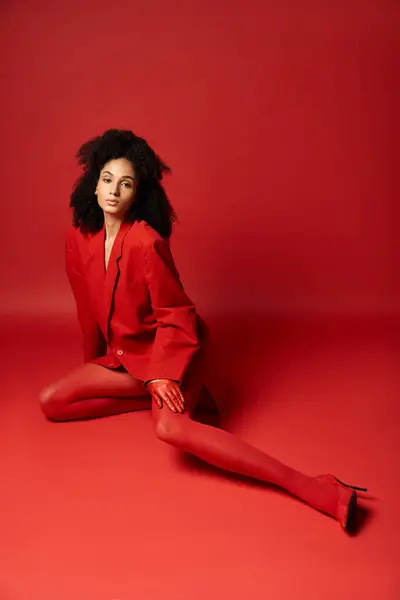A young woman exquisitely dressed in a red suit and tights sitting gracefully on the vibrant studio floor. — Stock Photo