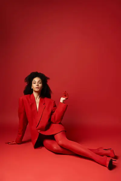 Uma jovem mulher em um terno vermelho vibrante sentada graciosamente no chão em um estúdio. — Fotografia de Stock