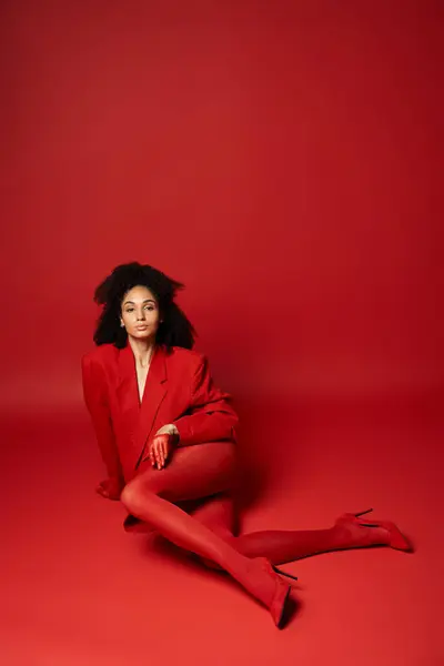 A young woman sits gracefully on the ground, wearing a bright red jacket and tights against a vibrant backdrop in a studio. — Stock Photo