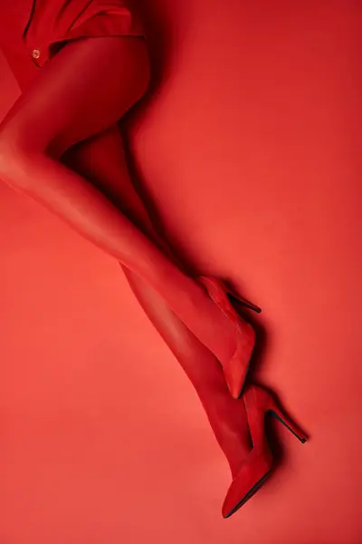 Una giovane donna con le gambe rivestite in calze rosse e tacchi alti, trasudando fiducia e fascino su un vibrante sfondo di studio. — Foto stock