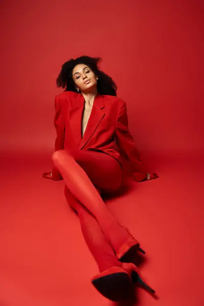 A young woman in a red suit sits gracefully on the vibrant red floor of a studio setting. — Stock Photo