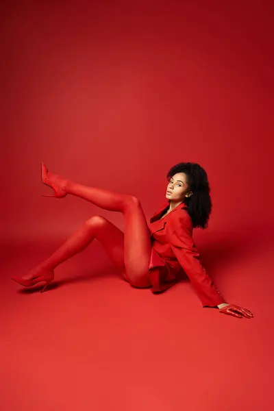 Молода жінка в яскраво-червоному костюмі лежить витончено на землі в студійній обстановці. — стокове фото
