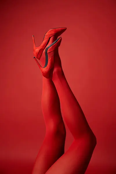 A young woman showcases her legs in tights against a bold red background, exuding strength and confidence. — Stock Photo