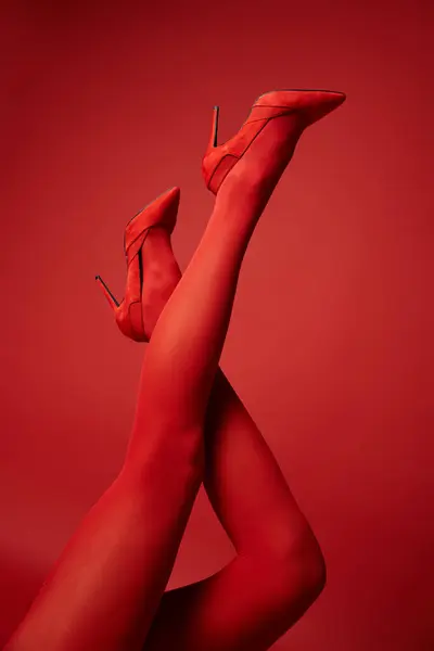 Eine junge Frau in roten Strümpfen und High Heels, die ihre Beine in einer verführerischen Pose vor einem lebendigen Studiohintergrund zur Schau stellt. — Stockfoto