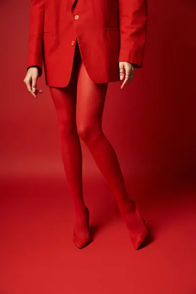 Uma mulher vestindo um terno vermelho vibrante e meia-calça fica em uma pose ousada e marcante. — Stock Photo