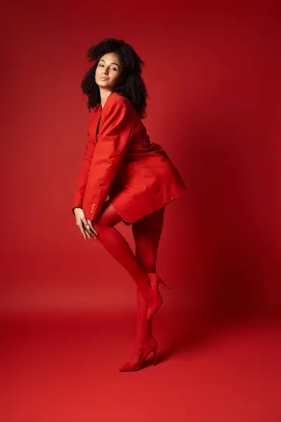 Una giovane donna trasuda eleganza in un abito rosso sorprendente, in posa per la fotocamera su uno sfondo vibrante studio. — Foto stock