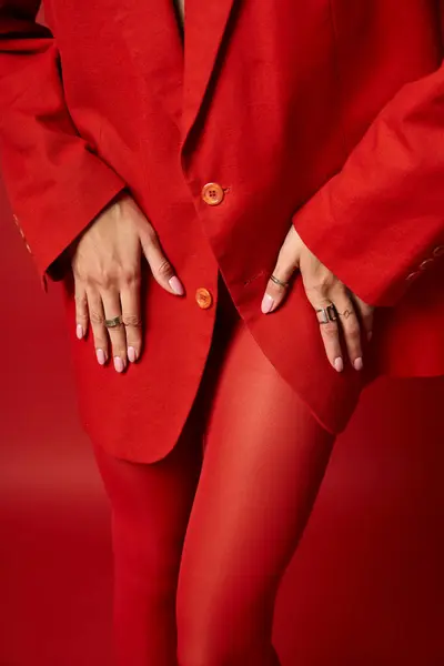 Eine stylische junge Frau steht selbstbewusst in rotem Anzug und passenden Strümpfen vor lebendigem Studiohintergrund. — Stockfoto