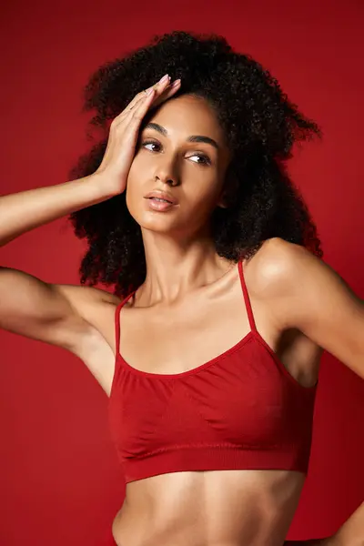 Jovem mulher vibrante confiantemente posa em um impressionante sutiã esportivo vermelho para uma fotocaça elegante. Configuração de estúdio. — Fotografia de Stock