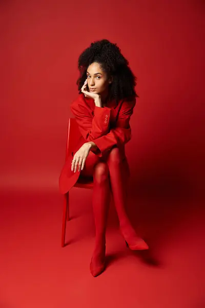 A stylish young woman in a vibrant red dress sits gracefully on a matching chair. — Stock Photo
