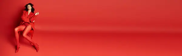 A young woman in a red dress stands elegantly against a matching vibrant red wall in a studio setting. — Stock Photo