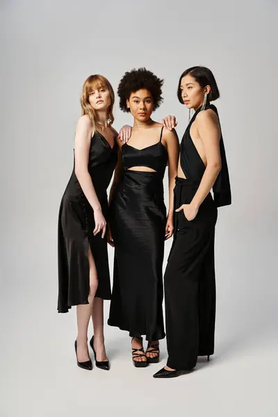 Three women of diverse backgrounds standing together elegantly against a grey studio backdrop. — Stock Photo