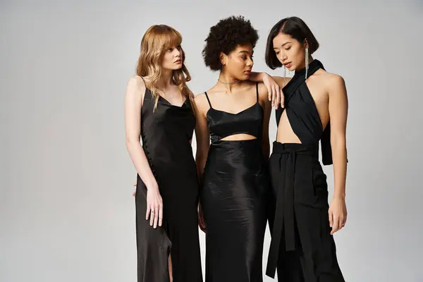 Trois femmes élégantes d'origine caucasienne, asiatique et afro-américaine se tiennent ensemble dans un décor de studio gris. — Photo de stock