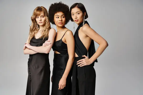 Три красиві жінки різних національностей витончено стоять разом на сірому фоні студії. — стокове фото