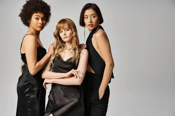 Three elegant women of Caucasian, Asian, and African American descent stand in unity on a grey studio backdrop. — Stock Photo