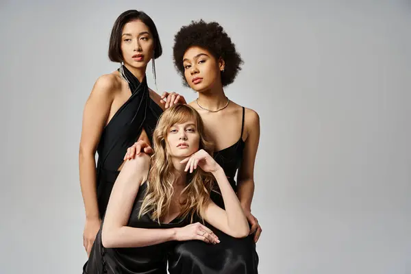 Tres diversas mujeres con vestidos negros posan sobre un fondo gris en un estudio. - foto de stock