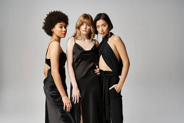 A group of three beautiful women of Caucasian, Asian, and African American descent standing gracefully together against a grey studio backdrop. — Stock Photo