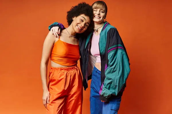 Duas mulheres bonitas de diferentes origens culturais que estão juntas em um estúdio contra um fundo laranja. — Fotografia de Stock