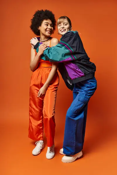 Une belle femme debout à côté d'un ami en pantalon orange sur un fond orange vif. — Photo de stock