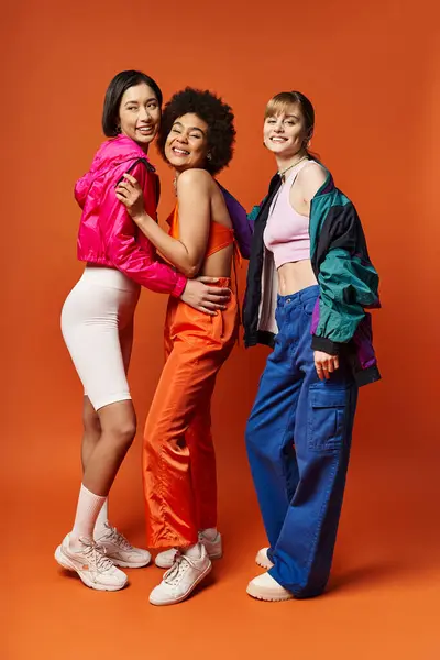 Tre belle donne di etnie diverse che stanno insieme su uno sfondo arancione. — Foto stock