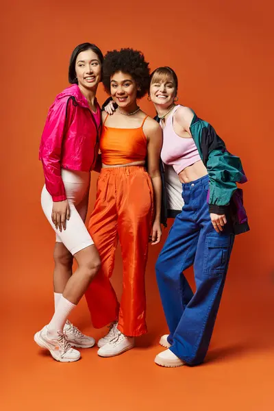 A diverse group of women standing together in front of an orange background, showcasing beauty and unity. — Stock Photo