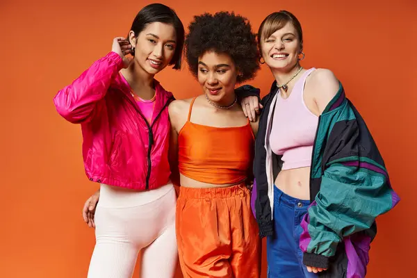 Três mulheres de diferentes etnias que estão juntas na frente de um fundo laranja, mostrando beleza multicultural e unidade. — Fotografia de Stock