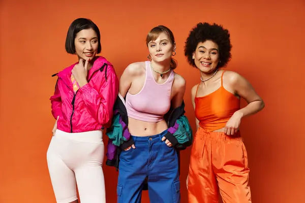 Three women of different ethnicities standing together, representing diversity and unity on a vibrant orange background. — Stock Photo