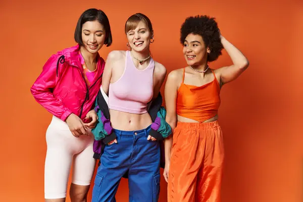 Drei unterschiedliche Frauen stehen Seite an Seite vor orangefarbenem Studiohintergrund und strahlen Schönheit und Ermächtigung aus. — Stockfoto